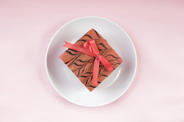 A Cake with A Red Ribbon on A White Plate on A Pink Background