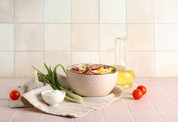 Bowl of tasty potato salad with onion and ingredients on pink tile table