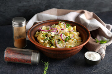 Bowl of tasty potato salad with onion and micro green on black background