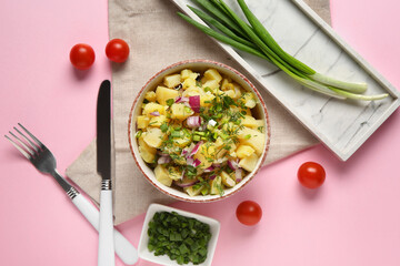 Bowl of tasty potato salad with onion and tomatoes on pink background