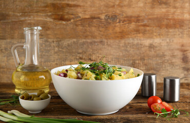 Bowl of tasty potato salad with onion, olives and tomatoes on wooden background