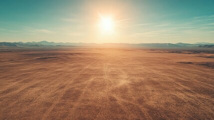Naklejka premium Expansive desert landscape under a bright sun with distant mountains and clear blue sky