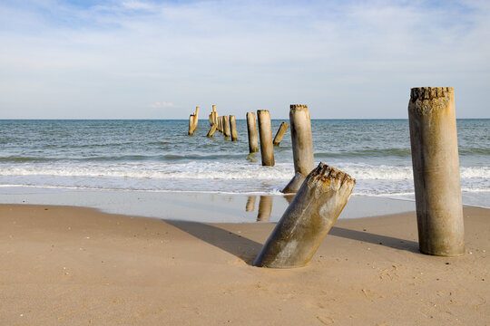 Cement pillar is located on  brown beach towards to the blue sea.