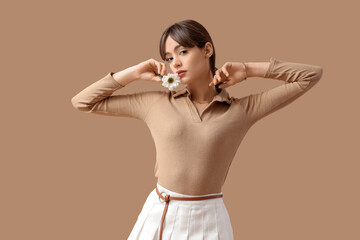 Pretty young woman in stylish outfit with flower on beige background