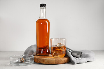 Bottle, glass of cold rum and ashtray on table against white background. Closeup