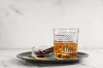 Glass of rum, orange slices and cigar in ashtray on plate on table against grey background. Closeup