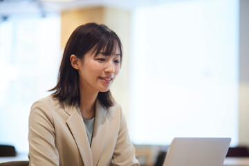 オフィス内でノートパソコンで仕事をする笑顔の日本人ビジネスウーマン