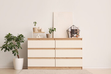 Interior of modern room with stylish dresser and houseplant near white wall