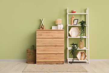 Interior of modern room with stylish dresser and shelving unit near green wall