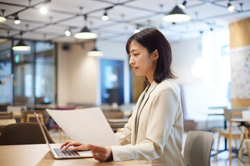 オフィス内でノートパソコンで仕事をする笑顔の日本人ビジネスウーマン