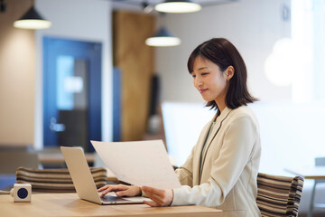 オフィス内でノートパソコンで仕事をする笑顔の日本人ビジネスウーマン