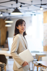 オフィスでノートパソコンを抱える笑顔の日本人女性のポートレート