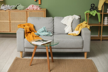 Interior of messy living room with sofa, commode and scattered clothes