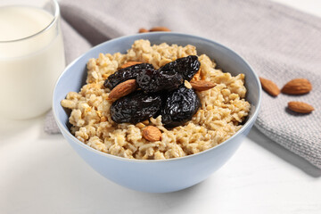 Bowl of tasty oatmeal with prunes, almonds and glass of milk on light background
