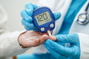 Asian doctor using digital glucose meter for check sample blood sugar level to treatment diabetes.