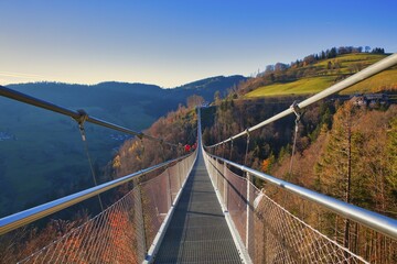 A suspension bridge leads over autumnal landscapes with hills in the background, Black Forest Line,...