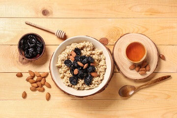 Bowl of tasty oatmeal with prunes, almonds and honey on light wooden background