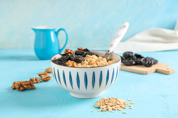 Bowl of tasty oatmeal with prunes, walnuts and spoon on blue grunge background