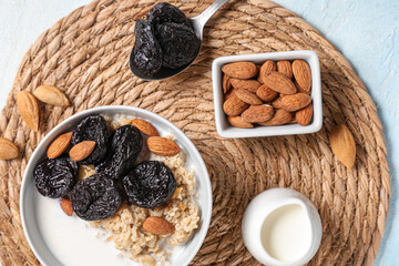 Bowl of tasty oatmeal with prunes, almonds and milk on light background