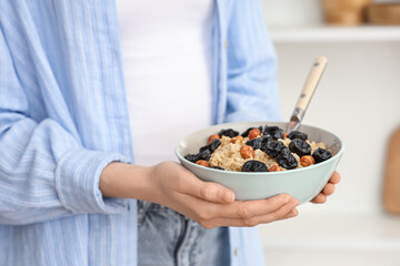 Woman holding bowl of tasty oatmeal with prunes, hazelnuts and spoon, closeup