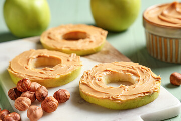 Board of tasty apple rounds with nut butter and hazelnuts, closeup