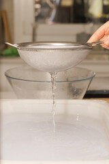 a woman's hand holding a strainer pouring water over a white pan