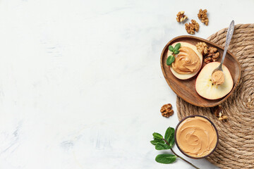 Wooden bowl with apple rounds, nut butter, walnuts and mint leaves on light background