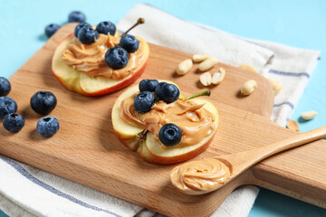 Wooden board with tasty apple slices, nut butter, blueberry and peanuts on blue background