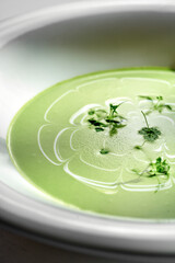 A close-up of a green pea soup, showcasing the creamy and smooth texture of the soup. The soup is garnished with fresh herbs and a swirl of cream