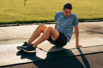 Young man performs bodyweight exercises on mat in park during sunny afternoon workout session