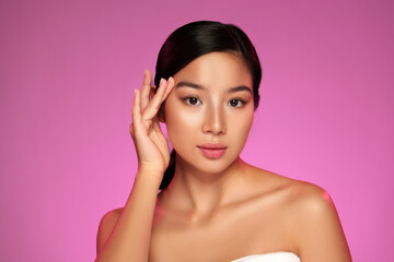 Model poses elegantly with a soft expression against a vibrant pink background in a beauty shoot