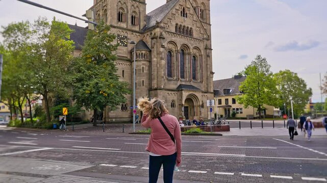Rear view of female tourist enjoying view of Herz-Jesu-Kirche Cathedral with birds flying overhead, Koblenz, Germany