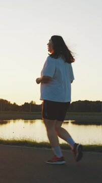 Motivated obese woman running along the river. Jogging for weight loss. Fat burning, running. Young unrecognizable overweight plus size woman jogging for weight loss. Weight loss, healthy lifestyle