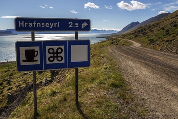 Signpost, gravel road meanders along a fjord through volcanic landscape, near Hrafnseyri,...