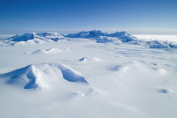 Aerial View of Antarctic Landscape: Pristine Snowdrifts and Majestic Mountains Under a Clear Blue Sky.