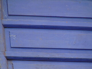 Close-up of a vibrant blue wooden door with textured panels and subtle scratches, creating a rustic and weathered aesthetic.