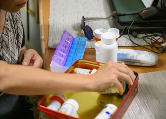 Woman sorting pills into medical pill boxes. Selective focus on pill boxes. California.
