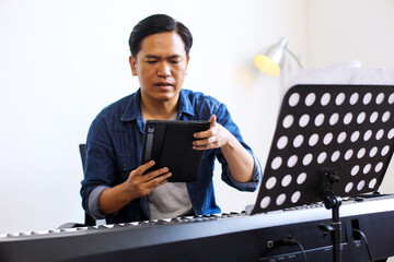 Man Playing Piano While Looking Digital Tablet at Home