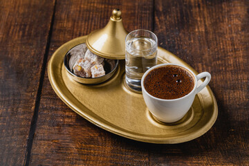 Turkish coffee in classic coffee cup with water and Turkish delight on wooden table