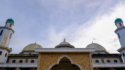 A low-angle, eye-level shot that captures the grandeur of the mosque's exterior against a partly cloudy, clear sky. The mosque showcases its architecture with its two towering minarets on either side.