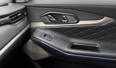 Door handle with power window control buttons. Black perforated leather interior with stitching. Modern car black leather interior details.