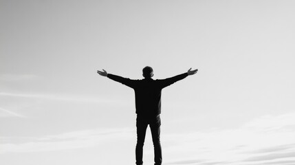 Man standing with outstretched arms against a bright sky.