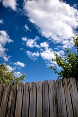 Fototapeta premium Wooden Fence Under a Blue Sky with Fluffy White Clouds: A Serene Landscape Photograph