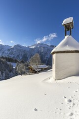 Fototapeta premium Mountain farm and chapel in winter, in Gerstruben, a former mountain farming village in the Dietersbach valley near Oberstdorf, behind it the Himmelschrofenzug, Allgäuer Alps, Allgäu, Bavaria, Germany.
