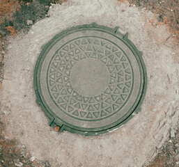 A round metal pipe with a green top sits on a patch of dirt
