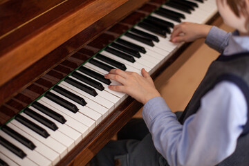 Fototapeta premium Close up of child's hands playing piano. Child learning to play music instrument. Development of musical abilities. Top view. Selective focus.