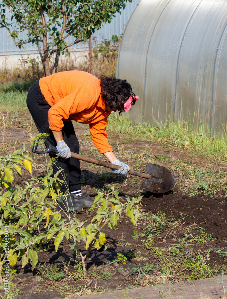 Wall mural A woman in an orange jacket is digging in the dirt with a shovel