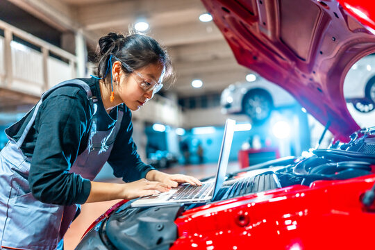 Female mechanic using laptop while inspecting car engine in auto repair shop