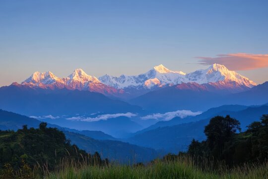 A breathtaking view of snow-capped mountains with soft morning light, misty valley, and a grassy foreground with wildflowers, perfect for adventure and travel - Powered by Adobe