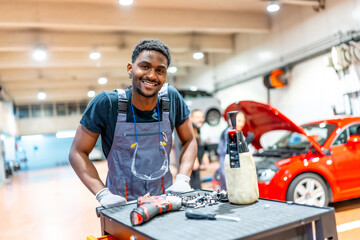 Smiling mechanic posing next to workbench in busy auto repair shop